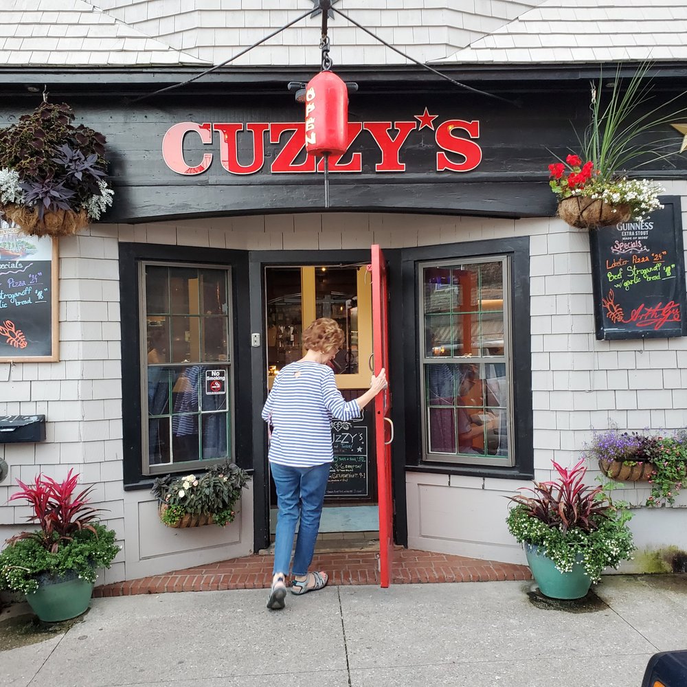 Cuzzy's - a woman opening the door of a restaurant - Pizza Near Me - Camden, Maine