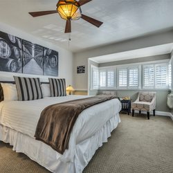 Craftsman Inn - King bed with white bedsheets, brown throw blanket, and two striped pillows. Two side tables and lamps. Wall art, ceiling fan, and TV.