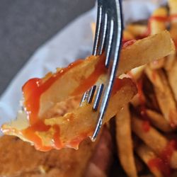 Village Grill - A fork holding a French Fries with ketchup.