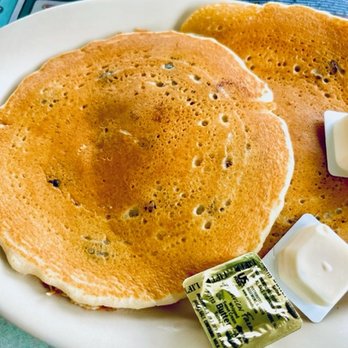 The Forked River Diner - a plate of pancakes - Two golden-brown pancakes with small dark spots are presented on a white plate, accompanied by butter and syrup packets. - American Near Me - Forked River, New Jersey