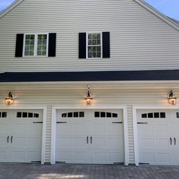 A white house features a three-car garage with decorative black window shutters and exterior wall-mounted lights.