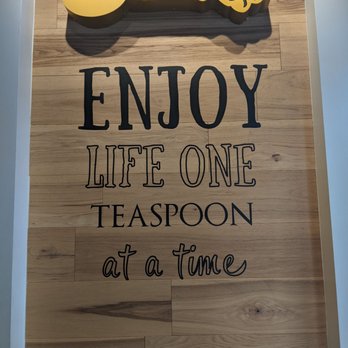 Teaspoon - Decor - A wall-mounted sign features a large yellow spoon above the phrase "Enjoy life one teaspoon at a time" on a wooden background, likely in a cafe or kitchen setting. - Bubble Tea Near Me - Davis, California