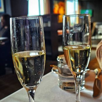 Zorba Lounge - Glass of champagne - Two flutes of champagne are placed on a table inside a restaurant or lounge with festive decorations and large windows. - Lounges Near Me - Naperville, Illinois