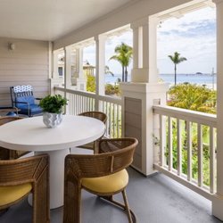 Large private covered terrace with outdoor dining table and seating overlooking the ocean and palm trees.
