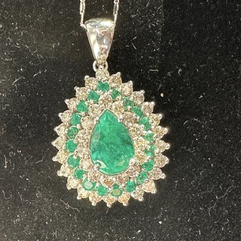 Humboldt Pawn - Wow! - The image shows a silver chain necklace with a large teardrop-shaped green gemstone pendant. The pendant is surrounded by multiple small clear stones and a ring of smaller green stones, creating a layered, ornate design. The necklace is displayed against a black textured background, highlighting the sparkle and color of the stones. - Jewelry Near Me - Eureka, California