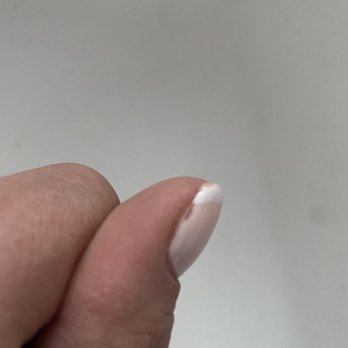Grace Nails 2 - Photo taken immediately after gel fill- 1/10/22 - The image depicts a close-up of a person's thumb, with the nail painted white. The nail polish is chipped at the tip, revealing the natural nail underneath. The background is plain and neutral, with no additional objects or details visible. - Nail Salons Near Me - Wolcott, Connecticut