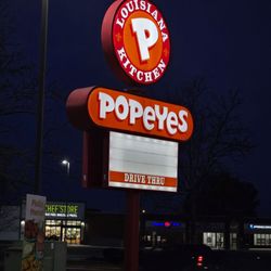 Popeyes Louisiana Kitchen - The lit parking lot sign of the restaurant at night.