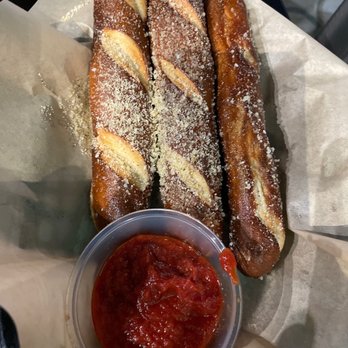 Missing Falls Brewery - Garlic parm pretzels - Three garlic parmesan pretzels sprinkled with cheese and served with a cup of marinara sauce, presented on parchment paper. - Breweries Near Me - Akron, Ohio