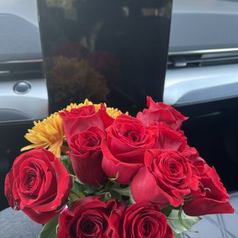 Trader Joe's - A hand holds a bouquet of red roses and yellow flowers inside a vehicle, with a car dashboard and a tablet mounted on the dashboard in the background. - Grocery Near Me - Concord, California