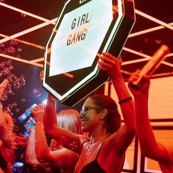 Trio - a woman holding up a sign in front of a crowd of people - Lounges Near Me - Charleston, South Carolina Trio - a woman holding up a sign in front of a crowd of people - Lounges Near Me - Charleston, South Carolina