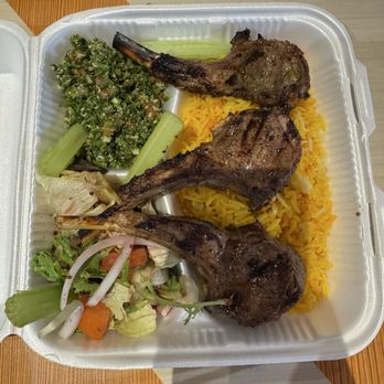 Kebab King - 10. Lamb Chops Plate - A foam takeout box contains grilled lamb chops, yellow rice, a mixed salad, and a vegetable side, served in a casual dining setting. - Middle Eastern Near Me - Tucson, Arizona