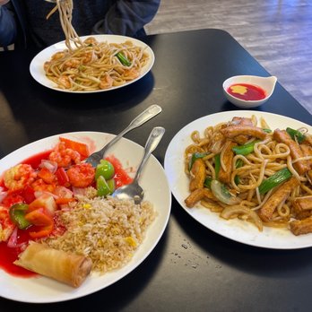 Lucky Wok - Sweet and 26. Sweet & Sour Shrimp Lunch Special 119. Japanese Noodle shrimp and tofu - Three dishes of Asian food are displayed on a black table: two plates of stir-fried noodles with vegetables and meat, and one plate of fried rice with shrimp, vegetables, and a spring roll. - Chinese Near Me - Albuquerque, New Mexico