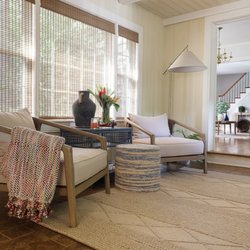 Designery Company - A warm, light-filled sitting room layered with natural textures, woven shades, neutral furnishings, and relaxed traditional charm.