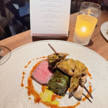 Canoe - A gourmet dish featuring sliced meat, stuffed vegetables, and sauce, served on a white plate in a restaurant setting with a candle and menu in the background. - Canadian (New) Near Me - Toronto, Ontario