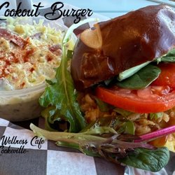 Juicys Wellness Cafe - Cookeville - "The Cookout Burger": Beyond Burger topped w/vegan mac & cheese, crispy onions, bbq sauce, cheddar cheese, & greens, all on a pretzel bun.
