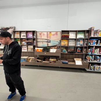 2nd Ave Thrift Superstore - A man wearing a black hoodie, black pants, and a black cap stands in front of bookshelves inside a store, looking at his phone. - Thrift Stores Near Me - Union, New Jersey
