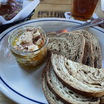 Notch Brewing - Czech marinated cheese with rye slices - A plate with several slices of multigrain bread, a small jar of honey, and a glass of iced tea on a wooden table. - Breweries Near Me - Salem, Massachusetts