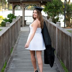 Khim Higgins Photography - Beautiful girl in a white dress holding her graduation gown walking away at Rollins College Campus.