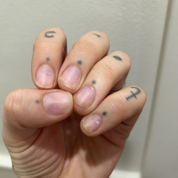 Oh La La Nail Spa - Sore nail pads, so thin. - A close-up of a hand with small tattoos on each finger and short, unpolished nails, clenched into a fist against a plain background. - Nail Salons Near Me - Elgin, Illinois