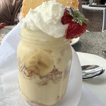 Pappadeaux Seafood Kitchen - Banana cream pudding - A layered dessert served in a glass jar, topped with whipped cream, fresh strawberries, and a large cookie, placed on a table. - Seafood Near Me - Albuquerque, New Mexico