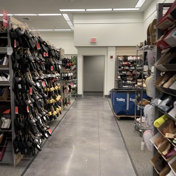 Nordstrom Rack - A retail store aisle with shelves stocked with shoes, handbags, and accessories on both sides, leading to an exit door. - Department Stores Near Me - Oak Brook, Illinois