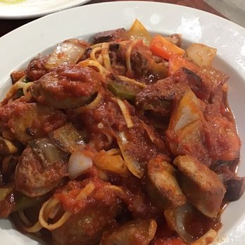 Vinny's Ristorante - Sausage Cacciatore with linguini - A plate contains sausage cacciatore with pasta, including chunks of sausage, potatoes, carrots, and onions in a tomato-based sauce. The dish is served on a white, round plate, with a small dish of olive oil and herbs visible in the background. The setting appears to be a restaurant with a wooden table surface. - Italian Near Me - Somerville, Massachusetts