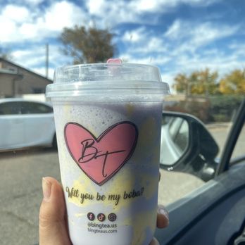 Bing Tea - Twisted Taro - A person holds a boba tea cup with a pink heart logo and the text 'Will you be my boba?' in front of a car window, with a blue sky and clouds visible outside. - Desserts Near Me - Albuquerque, New Mexico