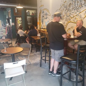 Montclair Brewery - Customers sit at tables and a high-top bar in a cafe or brewery, with a mural on the wall depicting abstract figures and objects. - Breweries Near Me - Montclair, New Jersey