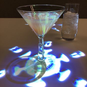 Electric Playhouse - Mocktails for everyone to start, even those who paid for alcohol pairings. Cute snowflakes but not interactive. - A martini glass with a colorful, iridescent drink and a tall glass of water with ice are on a table with light reflections and patterns. - Party & Event Planning Near Me - Albuquerque, New Mexico