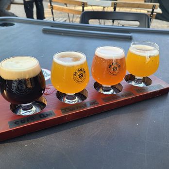 Magic 13 Brewing - Four craft beers are served in small glasses on a wooden paddle at Magic 13 Brewing, Miami, with a black table and outdoor seating in the background. - Breweries Near Me - Miami, Florida
