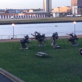 Royal Albert DLR Station - Early morning rower passing the statues of Newham Council, view from the station platform - Train Stations Near Me - Greater London, XGL