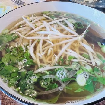 Pho6 - Braised short ribs pho - A bowl of Vietnamese pho featuring bean sprouts, chopped green onions, and fresh herbs in clear broth, with a black spoon on the side. - Szechuan Near Me - Mahopac, New York