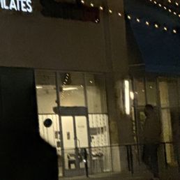 Closed - A person is seen standing outside a closed business at night, with illuminated signs and string lights visible on the building.