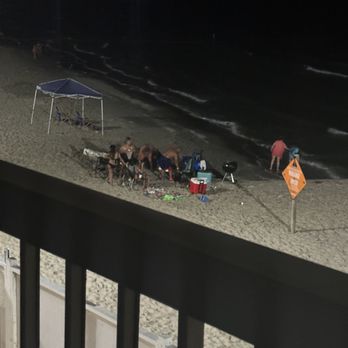 Emerald Beach Hotel - Orange biohazard water sign along with people partying/bbq at midnight on the beach - Hotels Near Me - Corpus Christi, Texas