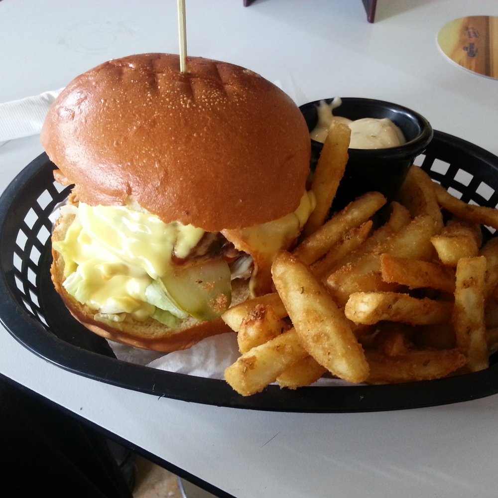 Angus Beef Burger, with streaky bacon, American cheese, pickles, iceberg lettuce, BBQ sauce, mustard mayo. Accompanied by fries and aioli.