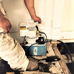 Delta Drainage & Foundation Repair - hydraulic Pier pushing machine, using inside an interior breakout in the home to complete Foundation Repair
