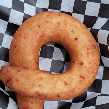 Sabe a zulia - Cornbread pretzel - A pretzel with a ring shape, resembling cornbread, featuring a golden-brown, crispy exterior with small reddish-brown spots. It is placed on black and white checkered paper, typical of casual food presentation, and appears freshly baked. - Venezuelan Near Me - Chicago, Illinois