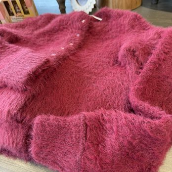 Uncharted - A pink fuzzy sweater with small decorative elements is laid out on a surface, with a background of furniture and decorative items. - Accessories Near Me - Oak Brook, Illinois