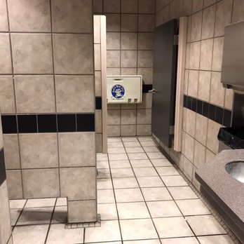 QuickTrip - Clean restrooms - The restroom has tiled walls and floors with a beige and black color scheme. A sink with a countertop is visible on the right side, along with a paper towel dispenser and a trash bin mounted on the wall. The space appears clean and well-maintained, with a door at the back leading to a stall or additional area. - Gas Stations Near Me - Mesa, Arizona