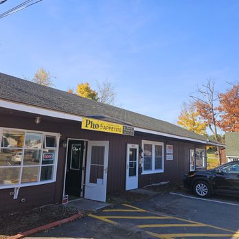 Pho Appetite - Outside - The image shows the storefront of Pho Appetite, a restaurant with a dark exterior, parking spaces, and autumn foliage in the background. - Vietnamese Near Me - Oakland, Maine