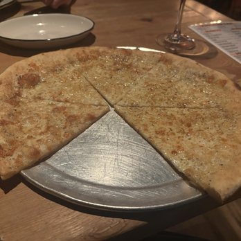 Taverna - Four cheese white pizza - A four cheese white pizza is served on a metal tray at a rustic Italian restaurant, with a wooden table and wine glass nearby. - Italian Near Me - Newark, Delaware
