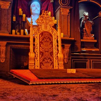 Mystique The Magic Experience - A decorative throne with intricate carvings is positioned in a dimly lit room, surrounded by statues and candles, creating a theatrical or ceremonial atmosphere. - Magicians Near Me - Mesa, Arizona