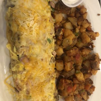 Pegah's - A breakfast plate featuring an omelet topped with shredded cheese, hash browns, and small containers of salsa and sour cream. - Salad Near Me - Lee's Summit, Missouri
