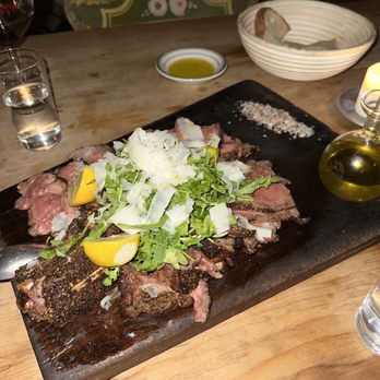 Il Buco - Bone in Ribeye with Arugula Salad on top. To the top right is rough salt for you to add to taste. - Italian Near Me - New York, New York Il Buco - Bone in Ribeye with Arugula Salad on top. To the top right is rough salt for you to add to taste. - Italian Near Me - New York, New York