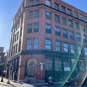 Lynn Vintage Warehouse - The warehouse - A brick building with multiple floors and large windows is situated on a city street corner, with street signs and parked cars visible. - Thrift Stores Near Me - Lynn, Massachusetts