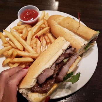 Froggy Bottom Pub - Pork bahn mi and fries - A plate containing French fries with ketchup, and two sandwiches with meat, vegetables, and bread, served on a dark wooden table. - Vietnamese Near Me - Washington, DC, District of Columbia