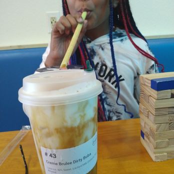 Feng Cha - A girl with multicolored braided hair is sipping a beverage through a large straw at a table, with a Jenga game nearby. - Coffee & Tea Near Me - Grapevine, Texas