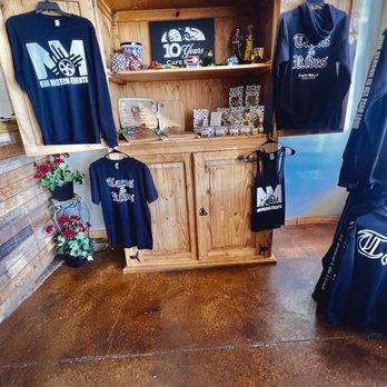 Cafe Bella Coffee - Merchandise - A wooden display shelf at Cafe Bella Coffee features branded clothing, souvenirs, and a 10-year anniversary sign, with decorative plants nearby. - Coffee & Tea Near Me - Rio Rancho, New Mexico