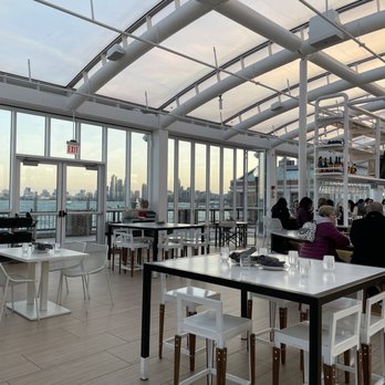 Offshore Rooftop - A rooftop restaurant features large glass windows, modern furniture, and a view of the city skyline, with patrons seated and enjoying drinks. - New American Near Me - Chicago, Illinois