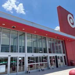 The entrance - Target retail store entrance featuring glass sliding doors, a red facade, and a Target logo sign on the building, with a clear sky overhead.